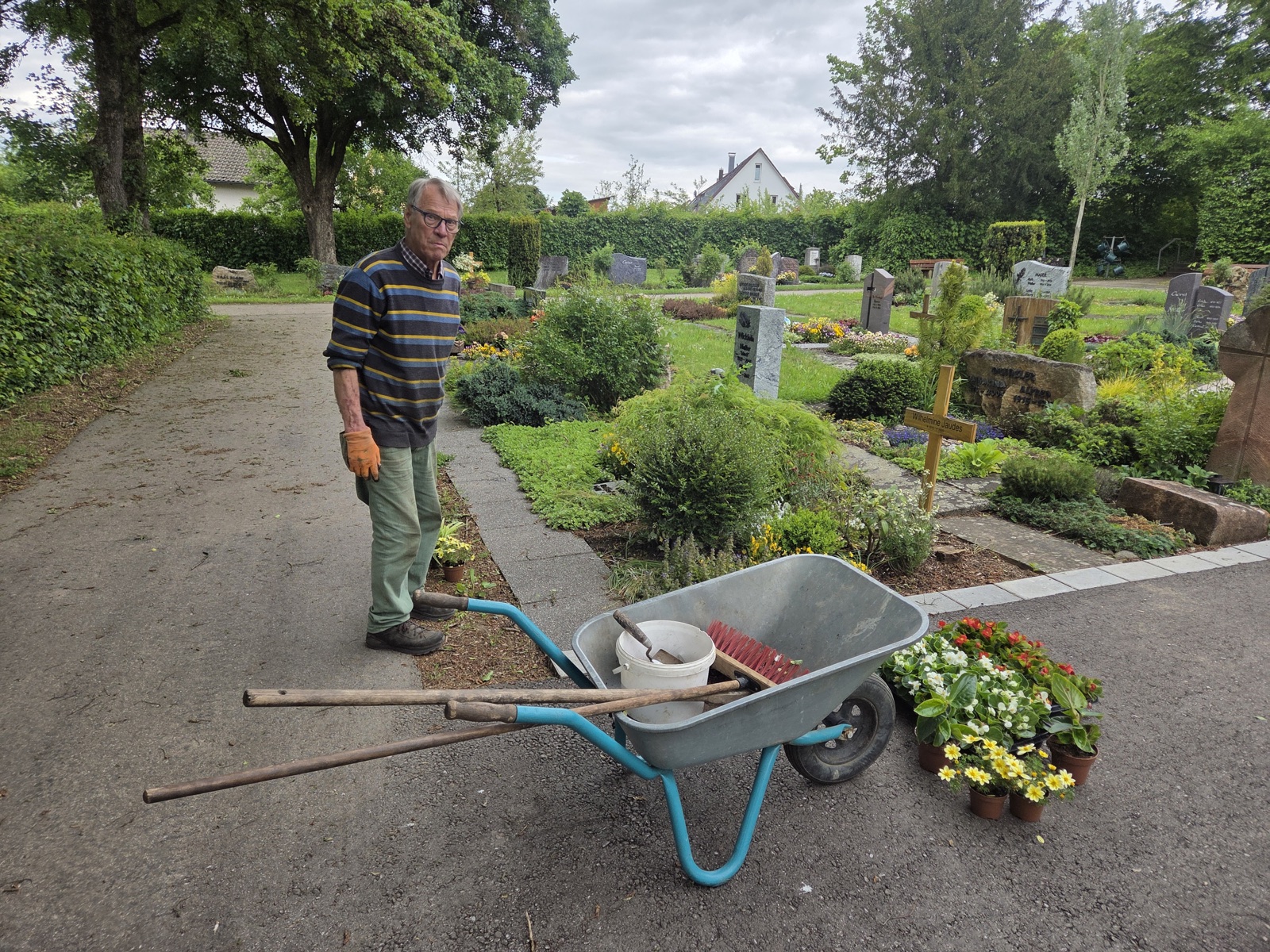 Gärtner der Gärtnerei Schanbacher mit Schubkarre, Werkzeug und Pflanzschalen bei der Grabpflege auf dem Friedhof Weiler