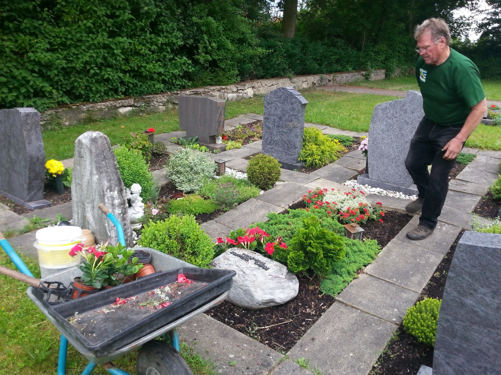 Gärtner der Gärtnerei Schanbacher bei der Bepflanzung eines Grab-Rundbeets mit Schubkarre auf dem Friedhof Weiler